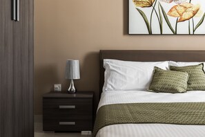 A bedroom with a bed, a nightstand, a lamp, and a painting on the wall.