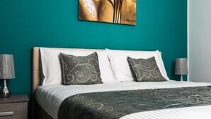A neatly made bed with patterned pillows and a decorative throw, a bedside lamp, and a wall-mounted abstract painting. - Portside Lodge Building (Marsaskala)