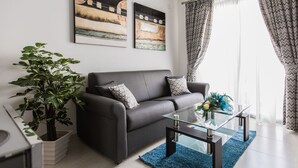 En moderne stue med en grå sofa, et glasbord og en potteplante.