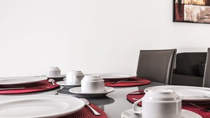Una mesa de comedor dispuesta con platos, tazones y vasos, con manteles individuales rojos y cubiertos.