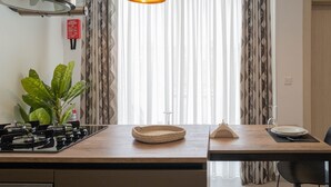 Una cocina con estufa a gas, una cesta tejida, una mesita con un plato y un vaso, y una planta en maceta.