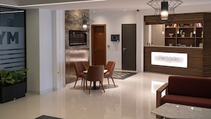A modern hotel lobby with a reception desk, seating area, and a large mirror. - Portside Lodge Building (Marsaskala)
