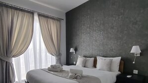 A modern bedroom with a bed, two bedside tables, a ceiling fan, and a large window with curtains. - Portside Lodge Building (Marsaskala)