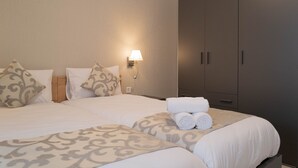 A hotel room with a bed, pillows, a nightstand, a lamp, and a wardrobe. - Portside Lodge Building (Marsaskala)