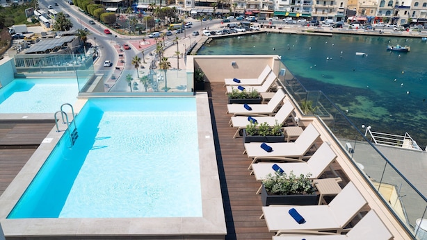Piscina no terraço com espreguiçadeiras e vista para o porto de iates.