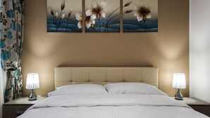 Una cama bien hecha con ropa blanca, flanqueada por dos lámparas de noche sobre mesitas a juego. Una obra de arte floral grande está centrada sobre la cama, y una cortina estampada se ve parcialmente a la izquierda.