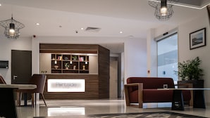 A modern reception area with a wooden reception desk, a red sofa, and a patterned rug. - Portside Lodge Building (Marsaskala)