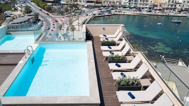 A rooftop pool with lounge chairs and a view of the marina. - Portside Lodge Building (Marsaskala)