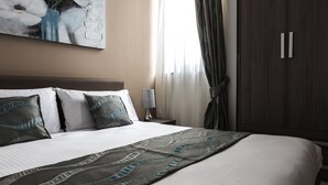 A neatly made bed with a patterned bedspread, a bedside lamp, and a large painting on the wall. - Portside Lodge Building (Marsaskala)