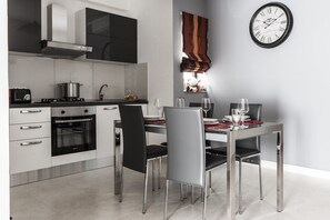A modern kitchen with stainless steel appliances, a dining table with chairs, and a wall clock.