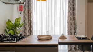 A kitchen with a gas stove, a woven basket, a small table with a plate and a glass, and a potted plant. - Portside Lodge Building (Marsaskala)