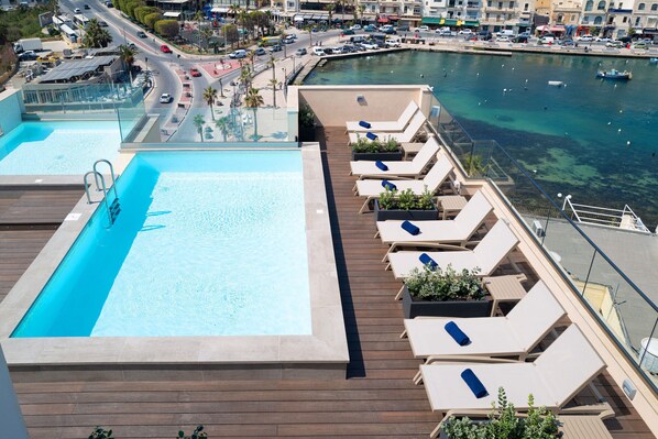 Une piscine sur le toit, dotée de chaises longues et offrant une vue sur le port de plaisance.