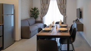 A modern kitchen with a dining area, a sofa, and a TV mounted on the wall. - Portside Lodge Building (Marsaskala)