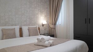 Ein Hotelzimmer mit geometrisch gemustertem Wandpapier, einem ordentlich bezogenen Bett mit aufgerollten Handtüchern, einer Nachttischlampe und einem Kleiderschrank.