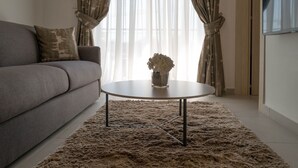 A living room with a grey sofa, a round coffee table with a vase, and a shaggy rug. - Portside Lodge Building (Marsaskala)
