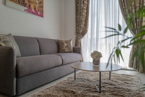 Uma sala de estar com um sofá cinza, uma mesa de centro redonda e um tapete felpudo.