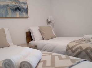 Habitación de hotel con dos camas, una mesita de noche, una lámpara y un cuadro en la pared.