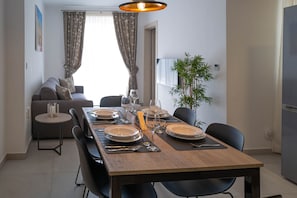 Uma sala de jantar com uma mesa de madeira posta para quatro pessoas, um sofá e uma planta.