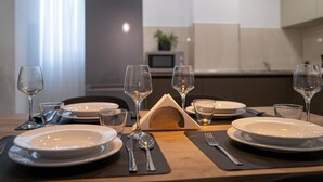 A dining table set with plates, cutlery, and wine glasses, with a microwave and cabinets in the background. - Portside Lodge Building (Marsaskala)