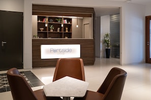A reception area with a 'Rent side LODGE' sign, a reception desk, a seating area with chairs and a table, and a bookshelf with various items.