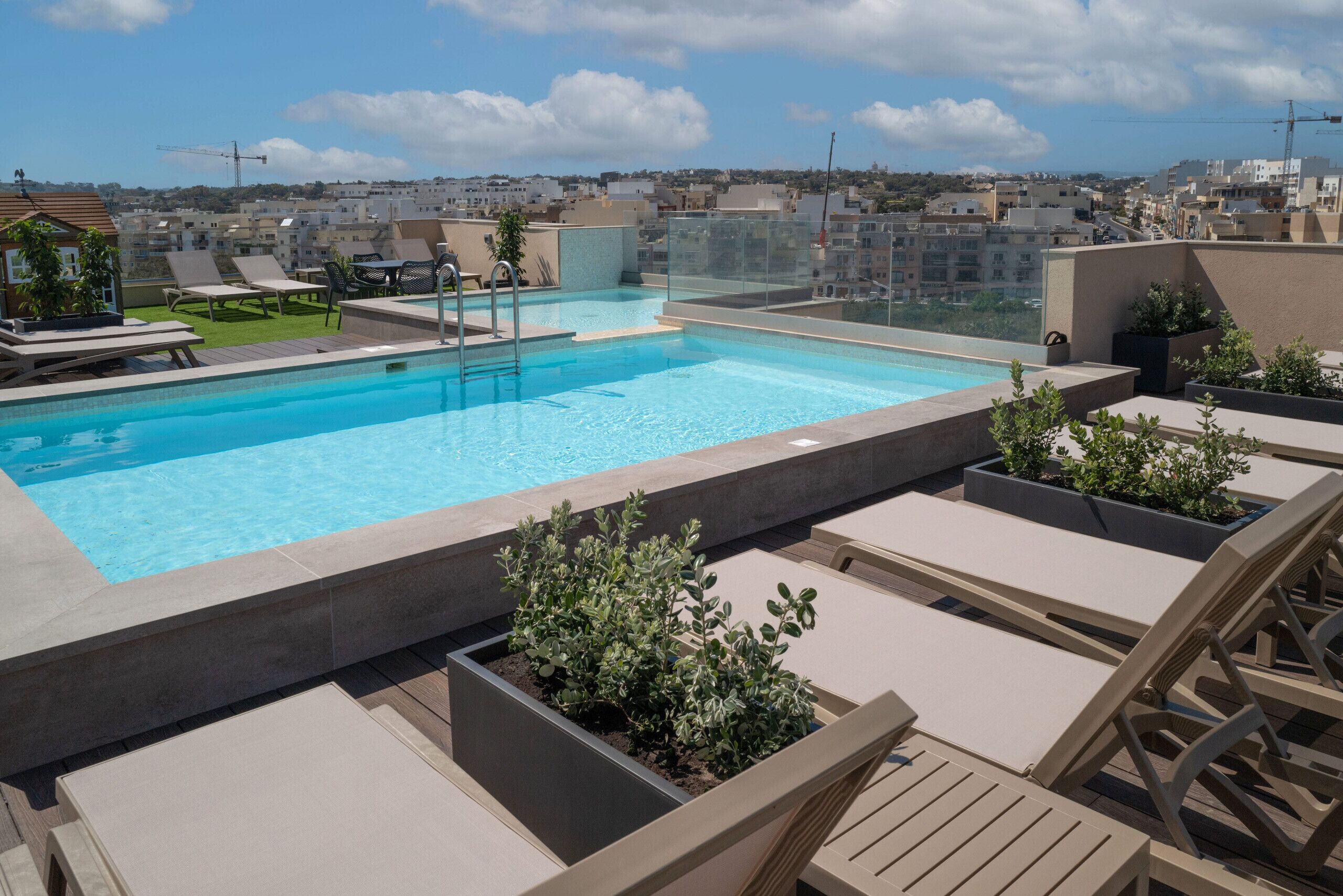 A rooftop pool with lounge chairs and planters, surrounded by a cityscape view.
