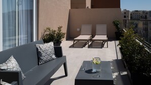 A rooftop terrace with a sofa, two lounge chairs, a table with a pitcher of water, and potted plants. - Portside Lodge Building (Marsaskala)
