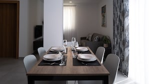 A dining area with a wooden table set for four, surrounded by white chairs. - Portside Lodge Building (Marsaskala)