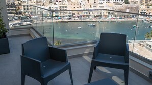 En balkon med to stole og et bord, der udover en lystbådehavn med både og et bybillede.