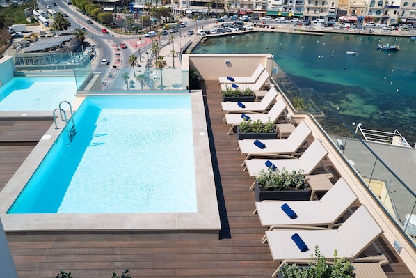 Une piscine sur le toit, dotée de chaises longues et offrant une vue sur le port de plaisance.