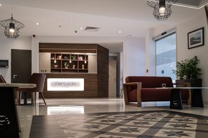 A modern reception area with a reception desk, a seating area with a sofa and chairs, a patterned rug, and a bookshelf with decorative items.