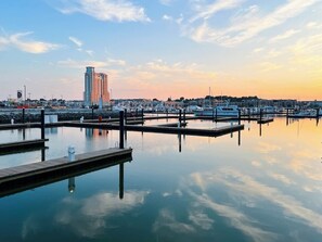A marina with docked boats, a tall building, and calm water reflecting the sky.