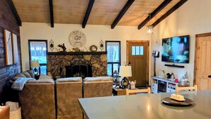 Un ampio soggiorno con camino in pietra, un orologio grande e una cucina moderna con TV a schermo piatto.