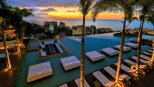 A rooftop infinity pool with lounge chairs, palm trees, and a sunset view of the ocean and cityscape. - Soho - PV
Luxury resort condo in heart of town with ocean & city view. (Puerto Vallarta)