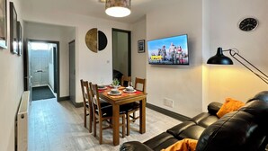Olohuone, jossa on ruokailutila, musta nahkasohva, seinälle asennettu televisio ja kattovalaisin.