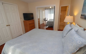 Un dormitorio con una cama, un televisor sobre un tocador, un espejo y una puerta.