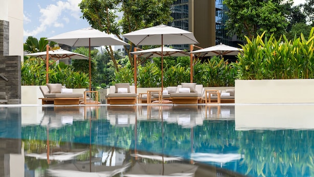 Un espace piscine agrémenté de chaises longues et de parasols, entouré d’une végétation luxuriante et de bâtiments modernes.