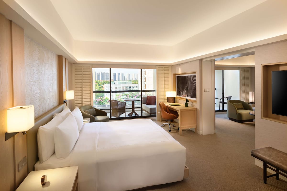 Hotelkamer met een groot bed, een bureau, twee stoelen, een televisie en een balkon met uitzicht op de stad.