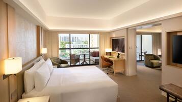 Habitación de hotel con una cama grande, un escritorio, dos sillas, televisor y un balcón con vistas a la ciudad.