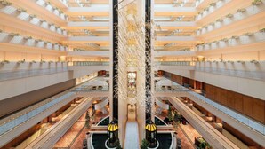 Un atrium à plusieurs niveaux, doté d’une allée centrale, de balcons ornés de plantes et d’un élément décoratif aquatique.