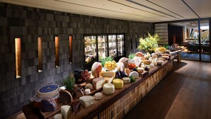 Une longue table de buffet garnie de différents fromages, de fruits et de fleurs.