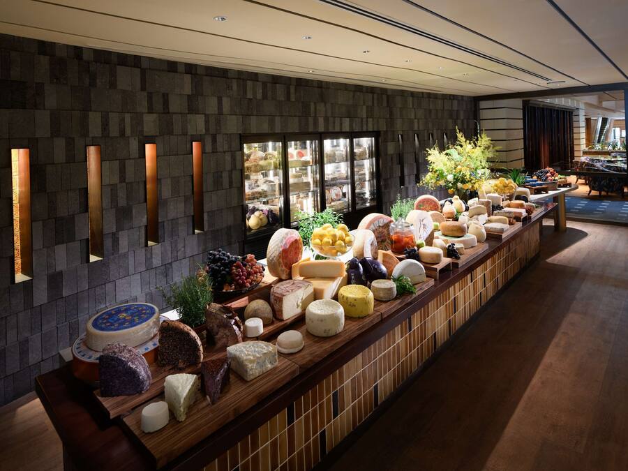 Una larga mesa de buffet con varios quesos, frutas y flores.