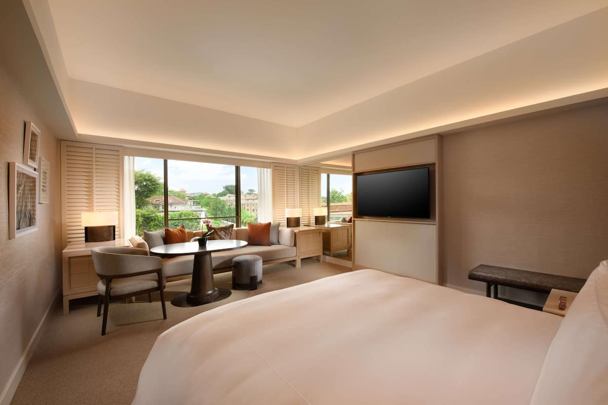 Een hotelkamer met een groot bed, een bureau met stoel, een bank, een televisie en grote ramen met uitzicht op het omliggende landschap.