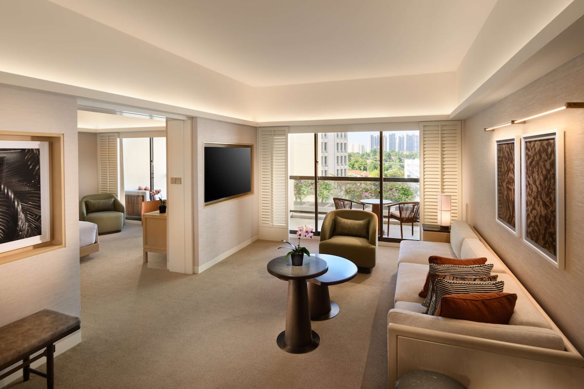 Een moderne hotelkamer met een zithoek, een flatscreen televisie, een bank, een salontafel en een balkon met uitzicht op de stad.