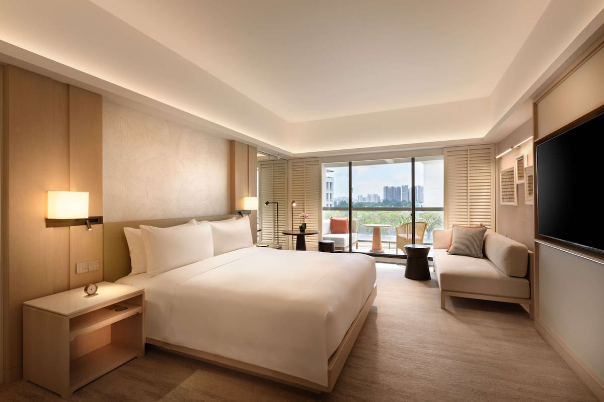 Een hotelkamer met een groot bed, een bank, een televisie en een balkon met uitzicht op de stad.