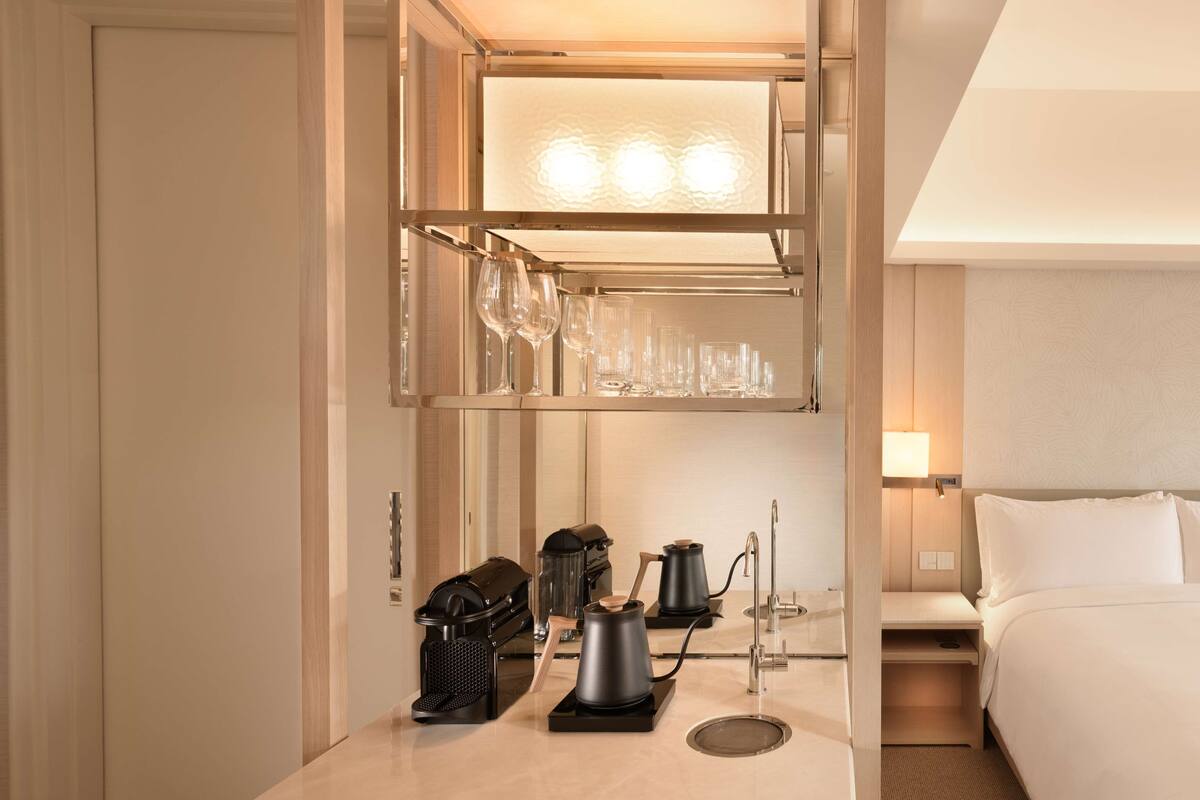 Hotelkamer met een minibar, koffiezetapparaat, waterkoker en een set glazen op een plank.