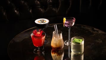 Una mesa redonda con cuatro bebidas distintas, un cuenco negro con diseño colorido y un sofá de cuero oscuro al fondo.