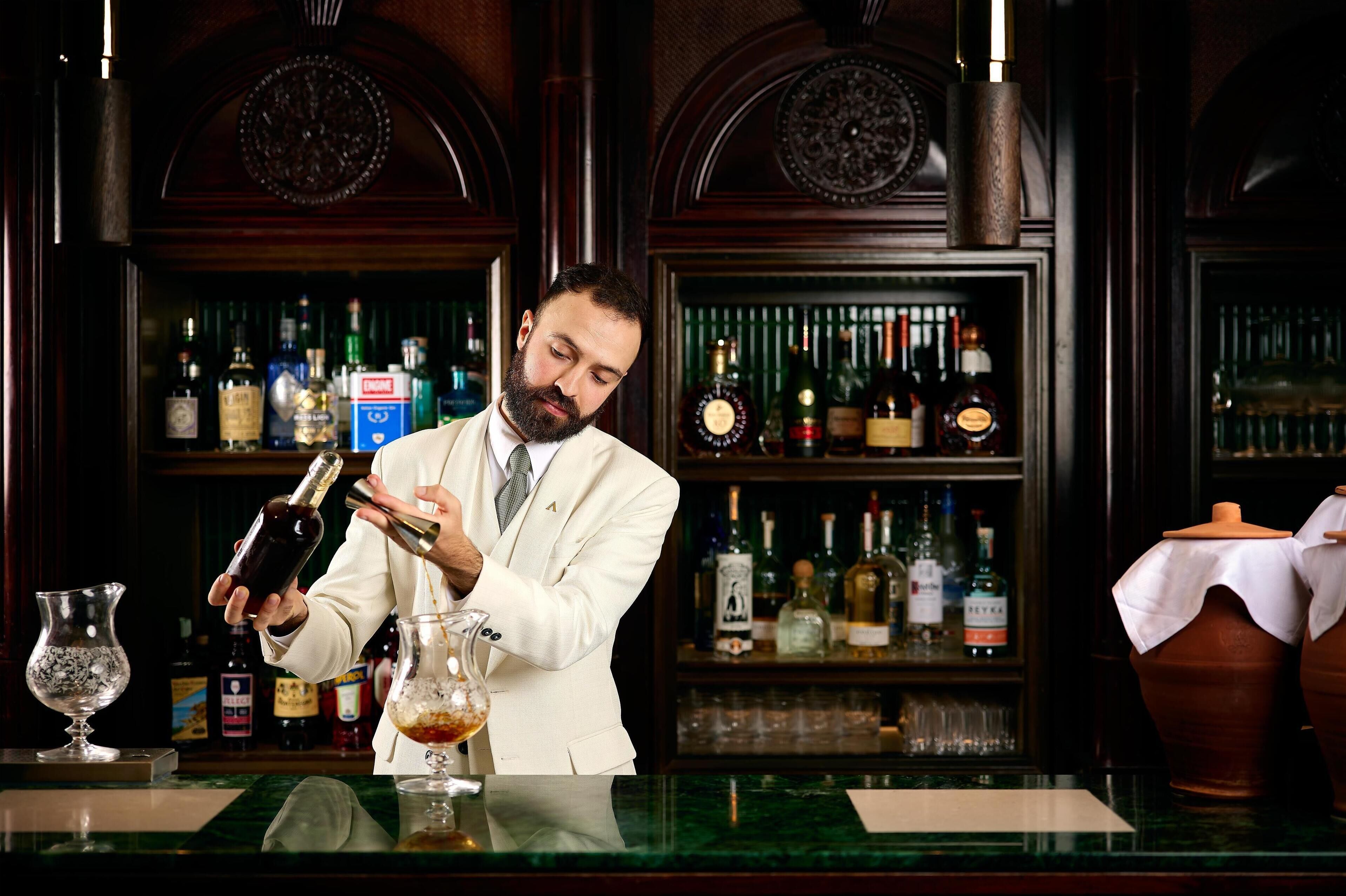 Een bar met een bartender die een drankje bereidt, drankflessen op planken en een bargedeelte.