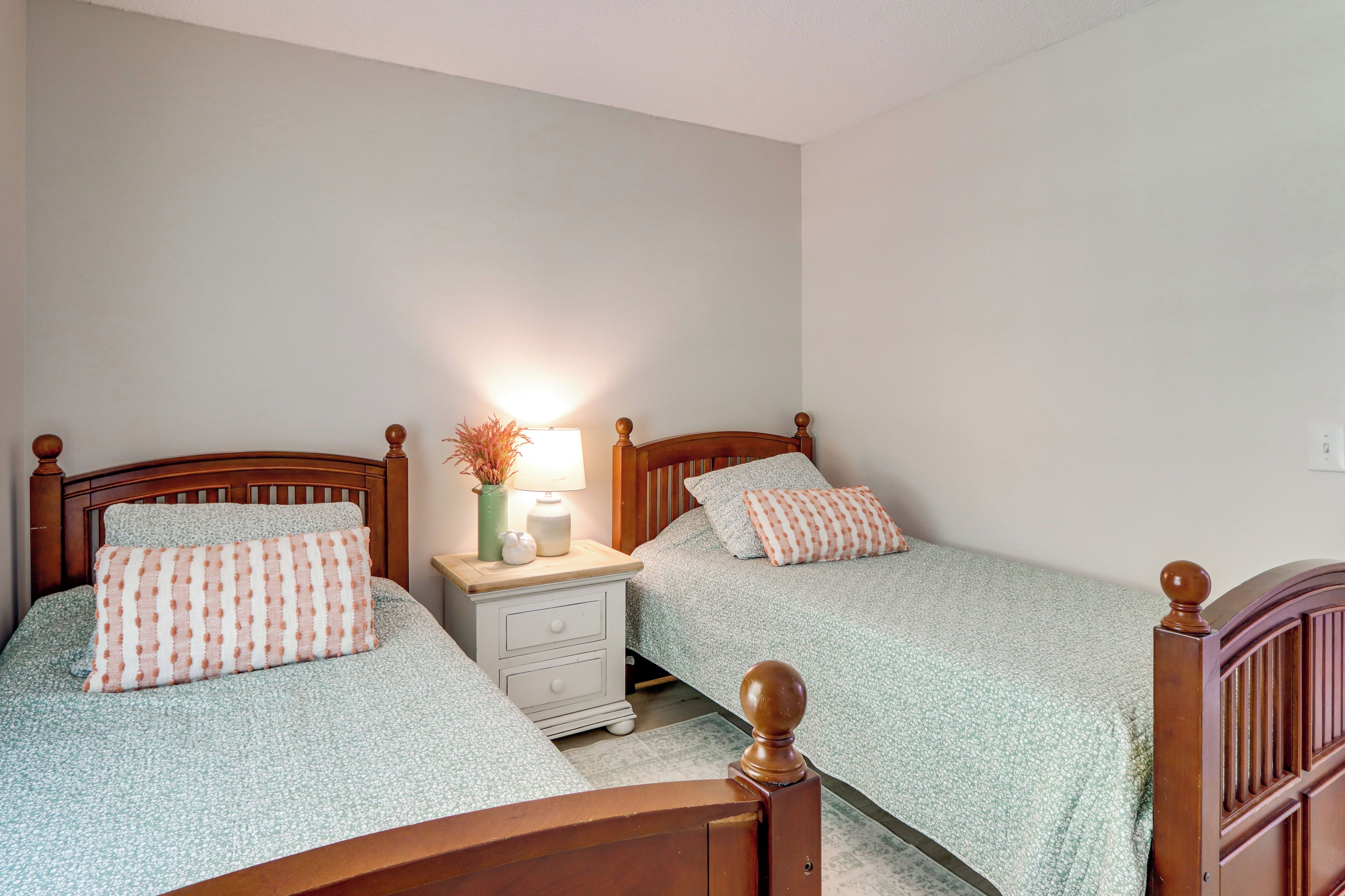 A bedroom with two single beds, a bedside table with a lamp, and a nightstand with a vase.