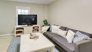 Ein Wohnzimmer mit Flachbildfernseher, einer Couch, einem Couchtisch und einem Fenster.
