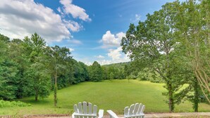 Zwei Adirondack-Stühle, die auf ein grünes Feld mit Bäumen im Hintergrund zeigen.